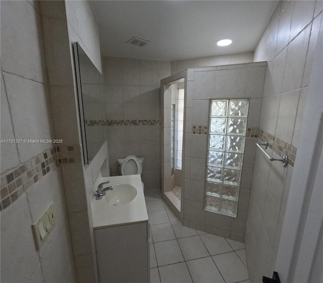 bathroom with tile walls, tile patterned flooring, vanity, a shower, and toilet