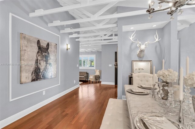 hall featuring lofted ceiling with beams, baseboards, and wood finished floors