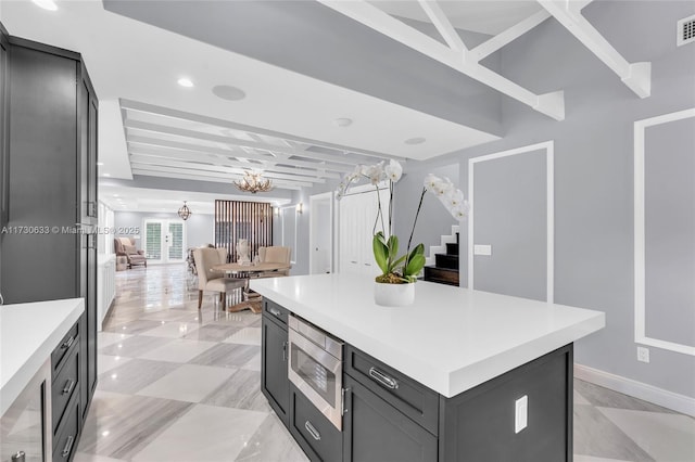 kitchen with stainless steel microwave, visible vents, an inviting chandelier, light countertops, and a kitchen island