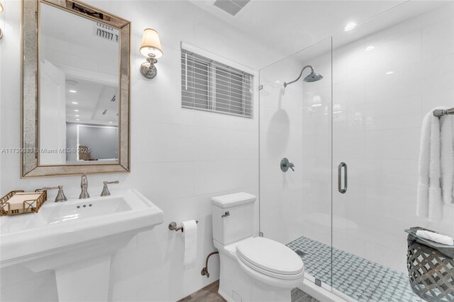 full bathroom featuring tile walls, toilet, visible vents, a sink, and a shower stall