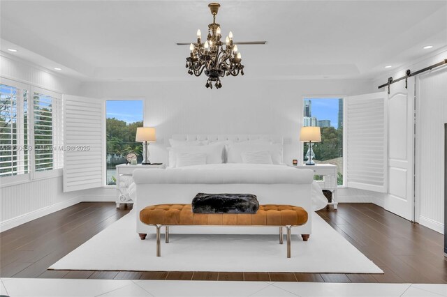 bedroom featuring a raised ceiling, a barn door, and dark hardwood / wood-style floors