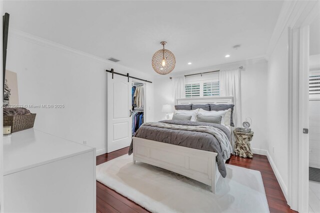 bedroom with dark hardwood / wood-style flooring, crown molding, a walk in closet, and a barn door