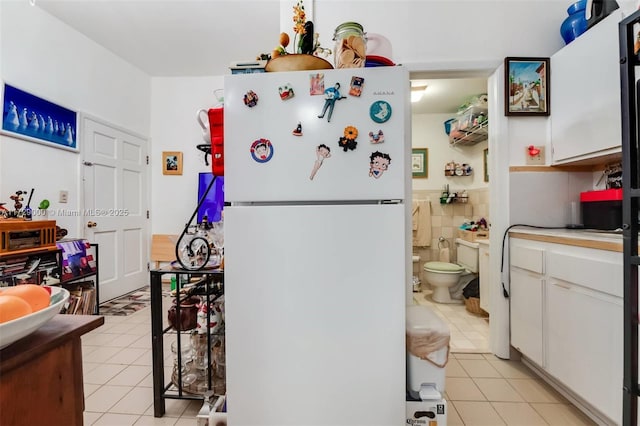 kitchen with white refrigerator, white cabinetry, tile walls, and light tile patterned floors