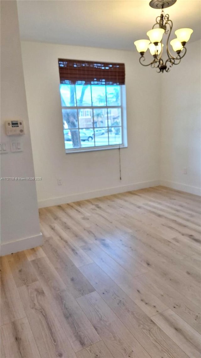 unfurnished room with a notable chandelier and light hardwood / wood-style floors