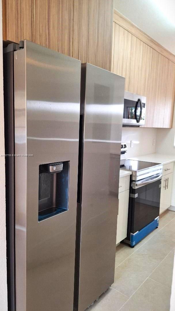 kitchen with stainless steel appliances, light tile patterned flooring, light brown cabinets, and white cabinetry