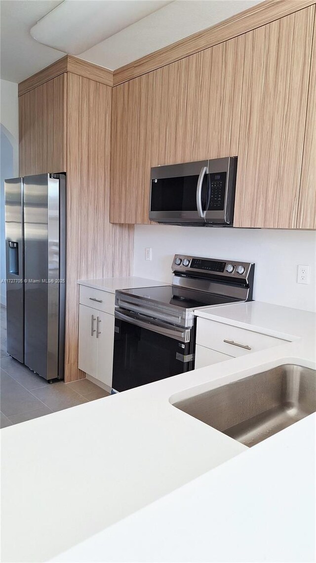 kitchen with stainless steel appliances, sink, light tile patterned floors, and light brown cabinets