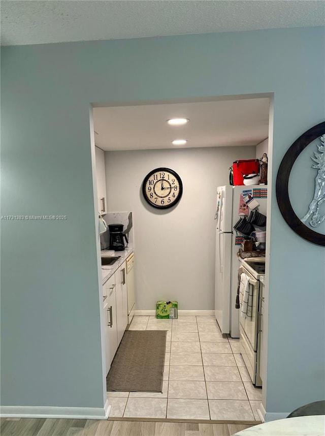 kitchen with white cabinetry, light tile patterned flooring, a textured ceiling, and white appliances