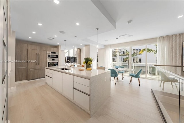 kitchen featuring pendant lighting, sink, white cabinets, stainless steel double oven, and a spacious island