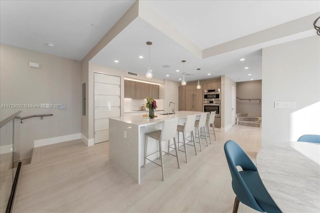 kitchen featuring sink, hanging light fixtures, an island with sink, stainless steel double oven, and white cabinets