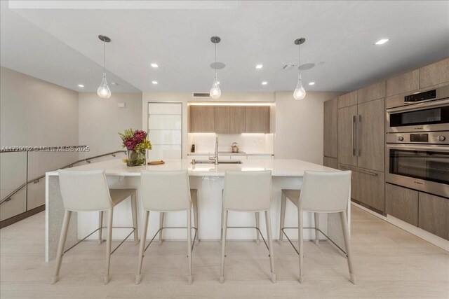 kitchen with a kitchen bar, sink, decorative light fixtures, stainless steel double oven, and a large island