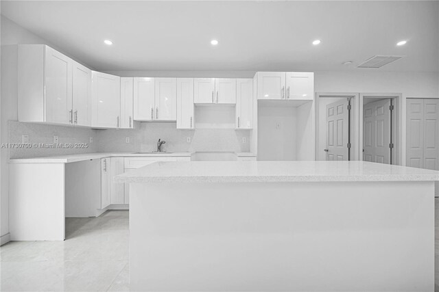 kitchen with tasteful backsplash, sink, white cabinets, and a kitchen island