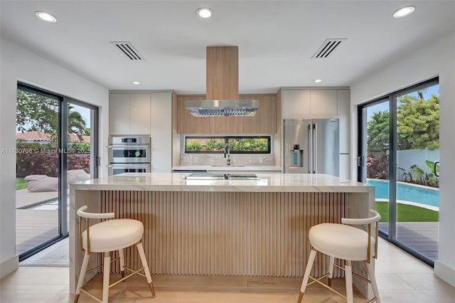 kitchen featuring island exhaust hood, appliances with stainless steel finishes, a healthy amount of sunlight, and a kitchen bar