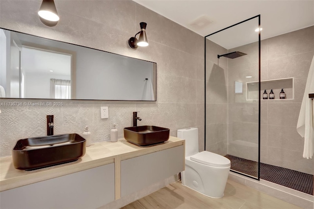 bathroom with tile walls, tiled shower, tasteful backsplash, vanity, and toilet