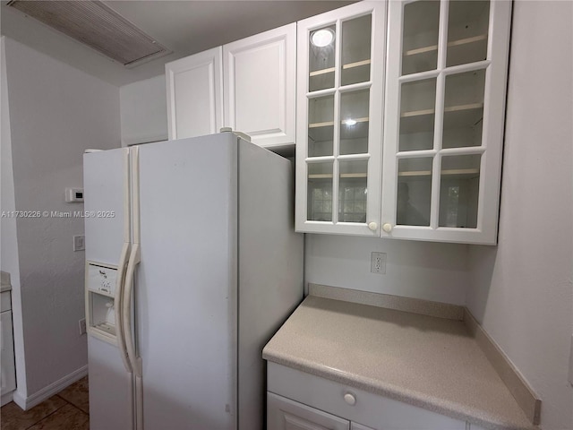 kitchen featuring white cabinetry, white refrigerator with ice dispenser, and dark tile patterned floors