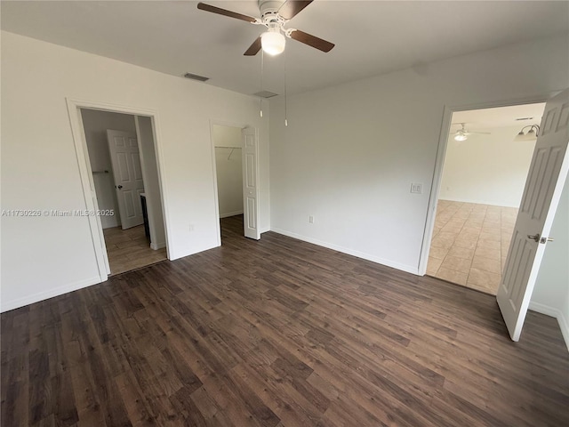 unfurnished bedroom with a walk in closet, dark wood-type flooring, ceiling fan, and a closet