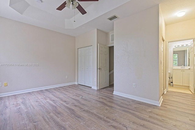 unfurnished bedroom with connected bathroom, sink, ceiling fan, light hardwood / wood-style floors, and a raised ceiling