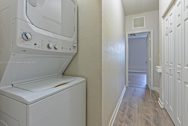 clothes washing area featuring stacked washer and clothes dryer, a textured ceiling, and light wood-type flooring