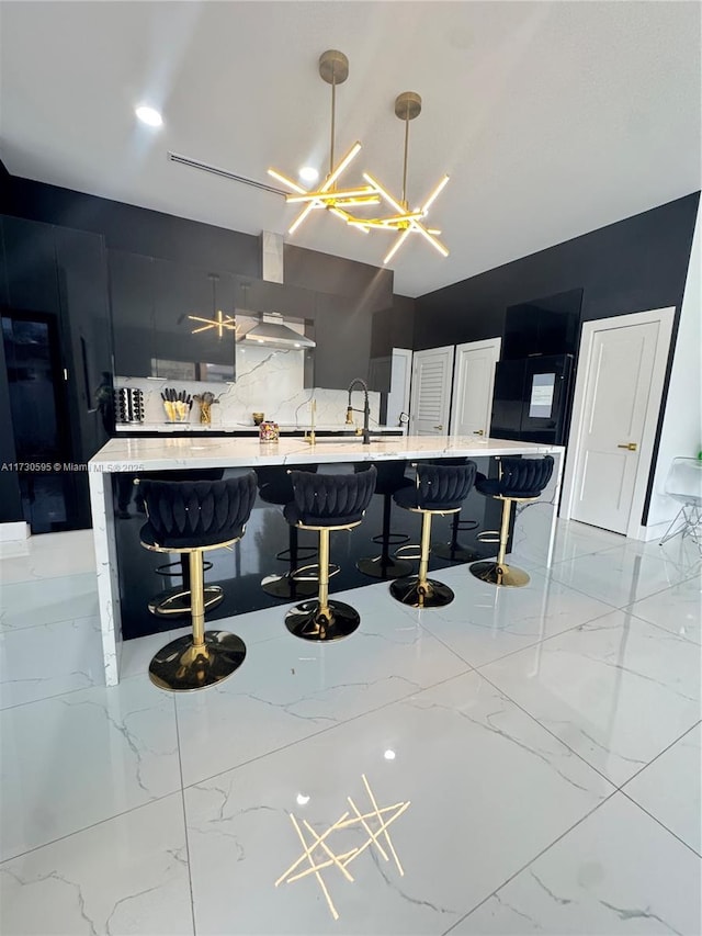 kitchen featuring pendant lighting, sink, wall chimney range hood, a breakfast bar, and backsplash