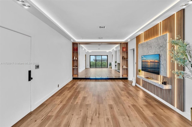 unfurnished living room featuring baseboards, built in shelves, visible vents, and light wood-style floors