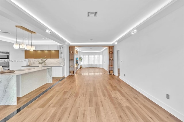 unfurnished living room featuring light wood finished floors, baseboards, visible vents, and a raised ceiling