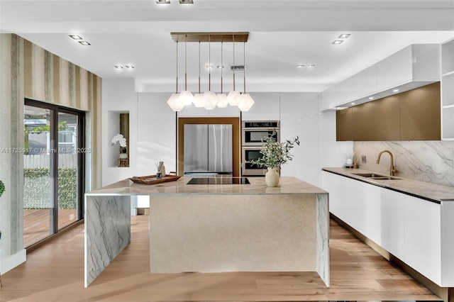 kitchen with appliances with stainless steel finishes, light wood-style floors, a kitchen island, a sink, and modern cabinets