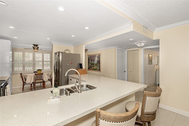 kitchen featuring light tile patterned flooring, sink, a breakfast bar area, crown molding, and stainless steel refrigerator