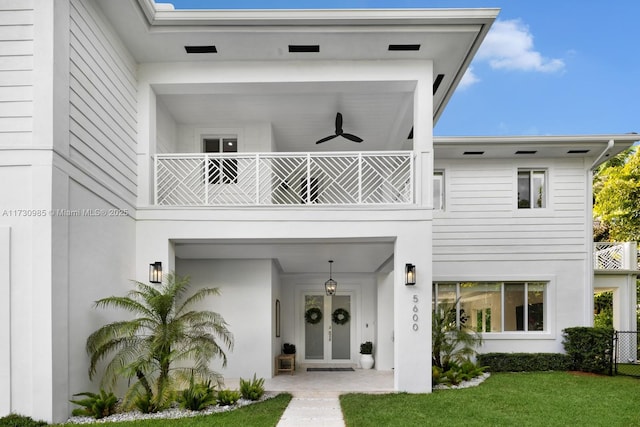 view of front of home featuring a front yard, a balcony, a ceiling fan, and stucco siding