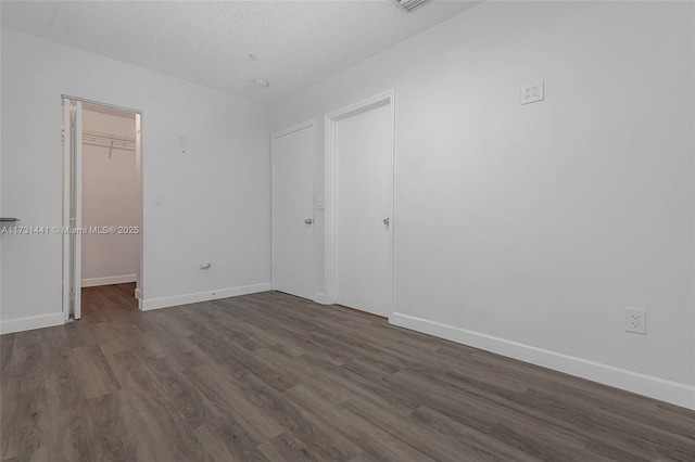 unfurnished bedroom with a walk in closet, dark wood-type flooring, a textured ceiling, and a closet