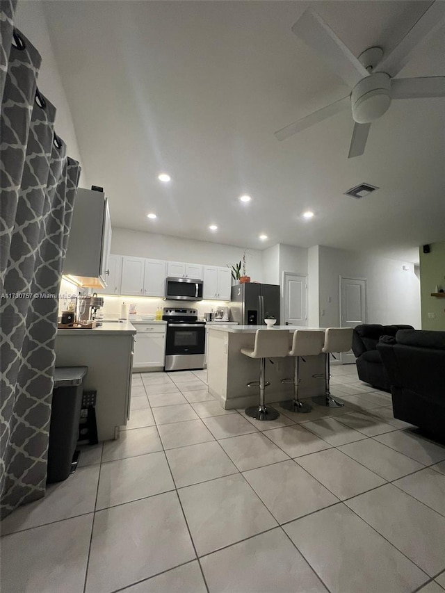 kitchen with light tile patterned floors, a kitchen breakfast bar, stainless steel appliances, a center island, and white cabinets