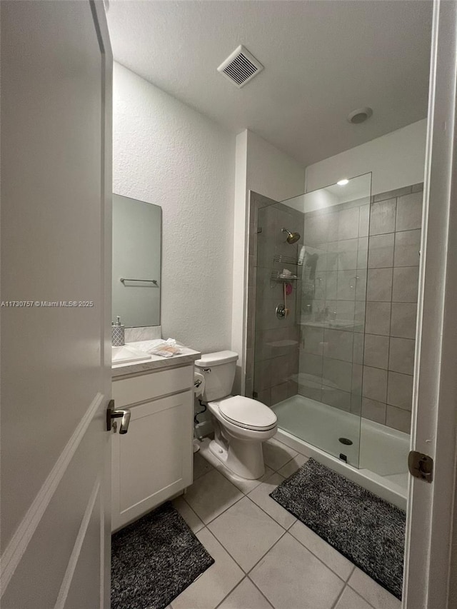 bathroom featuring tile patterned floors, toilet, vanity, and a tile shower