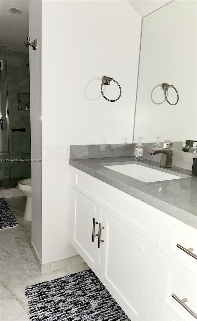 bathroom featuring toilet, vanity, and a shower with shower door