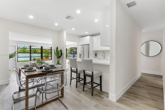 kitchen with a breakfast bar, white cabinetry, stainless steel fridge, kitchen peninsula, and light wood-type flooring