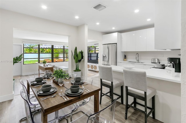 kitchen with stainless steel refrigerator with ice dispenser, sink, white cabinetry, a kitchen breakfast bar, and kitchen peninsula