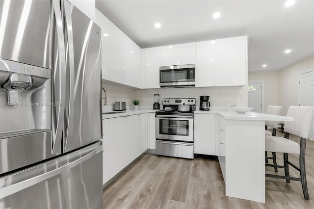 kitchen featuring a breakfast bar, appliances with stainless steel finishes, kitchen peninsula, light hardwood / wood-style floors, and white cabinets