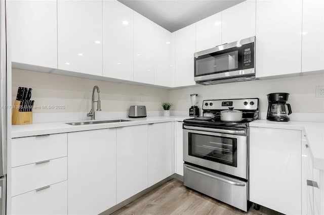 kitchen featuring sink, light hardwood / wood-style floors, white cabinets, and appliances with stainless steel finishes