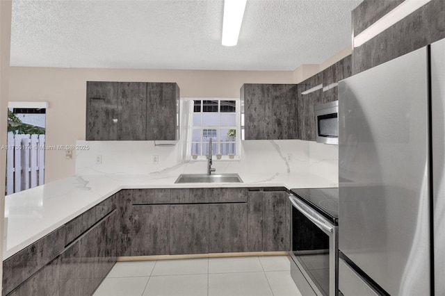 kitchen featuring sink, a textured ceiling, light tile patterned floors, stainless steel appliances, and light stone countertops