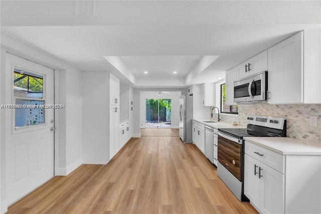 kitchen with sink, white cabinetry, a raised ceiling, stainless steel appliances, and decorative backsplash