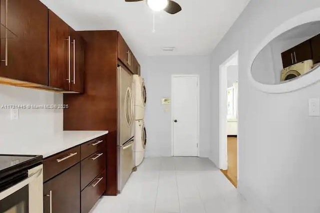 kitchen with stacked washer and clothes dryer, dark brown cabinets, light tile patterned floors, stainless steel refrigerator, and ceiling fan