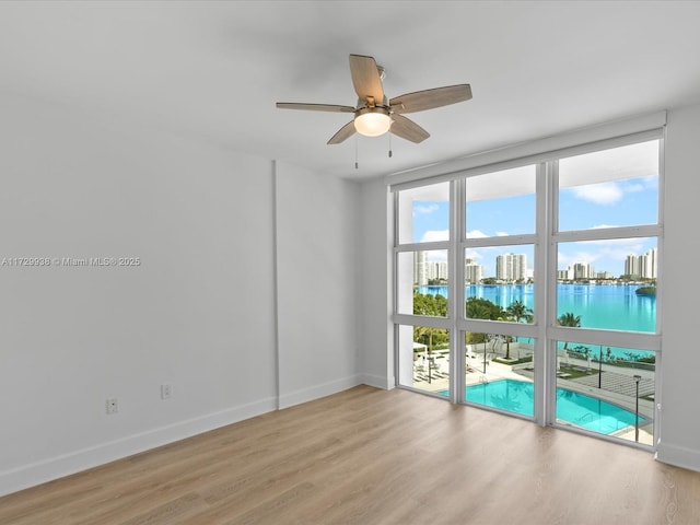 spare room featuring ceiling fan, a wall of windows, and light wood-type flooring