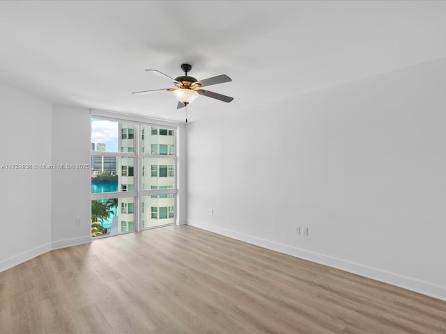 spare room with ceiling fan, a wall of windows, and light hardwood / wood-style floors