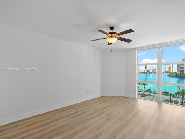 unfurnished room featuring light wood-type flooring, expansive windows, ceiling fan, and a water view