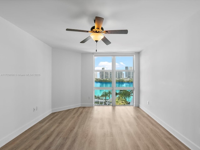 unfurnished room with ceiling fan, a water view, light hardwood / wood-style floors, and a wall of windows