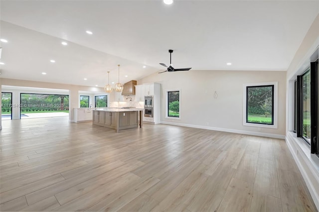 unfurnished living room featuring lofted ceiling, ceiling fan with notable chandelier, light hardwood / wood-style floors, and a healthy amount of sunlight