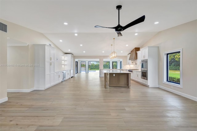 kitchen featuring decorative light fixtures, a kitchen breakfast bar, a kitchen island, white cabinets, and wall chimney range hood