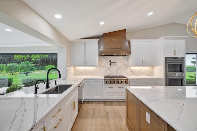 kitchen with appliances with stainless steel finishes, lofted ceiling, sink, white cabinets, and custom exhaust hood