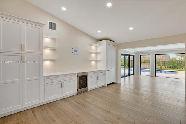 kitchen with light hardwood / wood-style flooring, white cabinetry, light stone countertops, vaulted ceiling, and beverage cooler