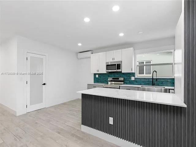 kitchen with a wall mounted air conditioner, sink, white cabinets, kitchen peninsula, and stainless steel appliances