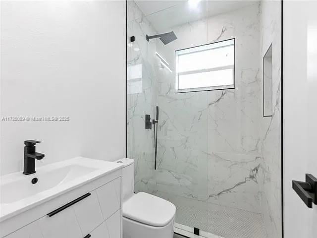 bathroom featuring vanity, tiled shower, and toilet