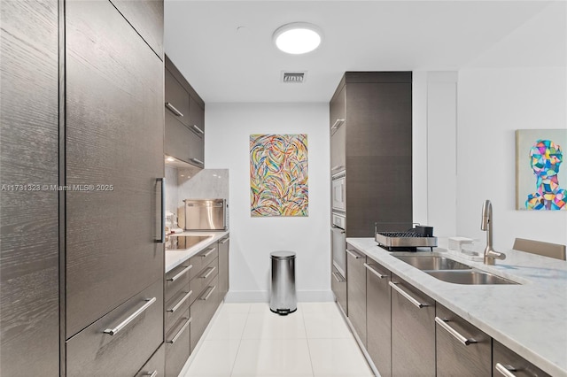 kitchen featuring sink, light tile patterned floors, stainless steel appliances, and light stone countertops