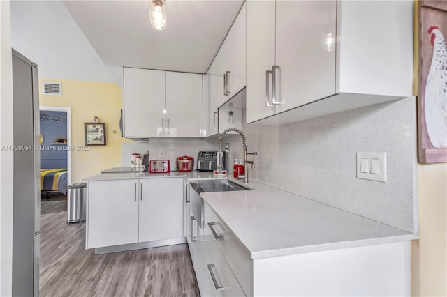 kitchen featuring sink, light hardwood / wood-style flooring, white cabinets, black electric stovetop, and backsplash